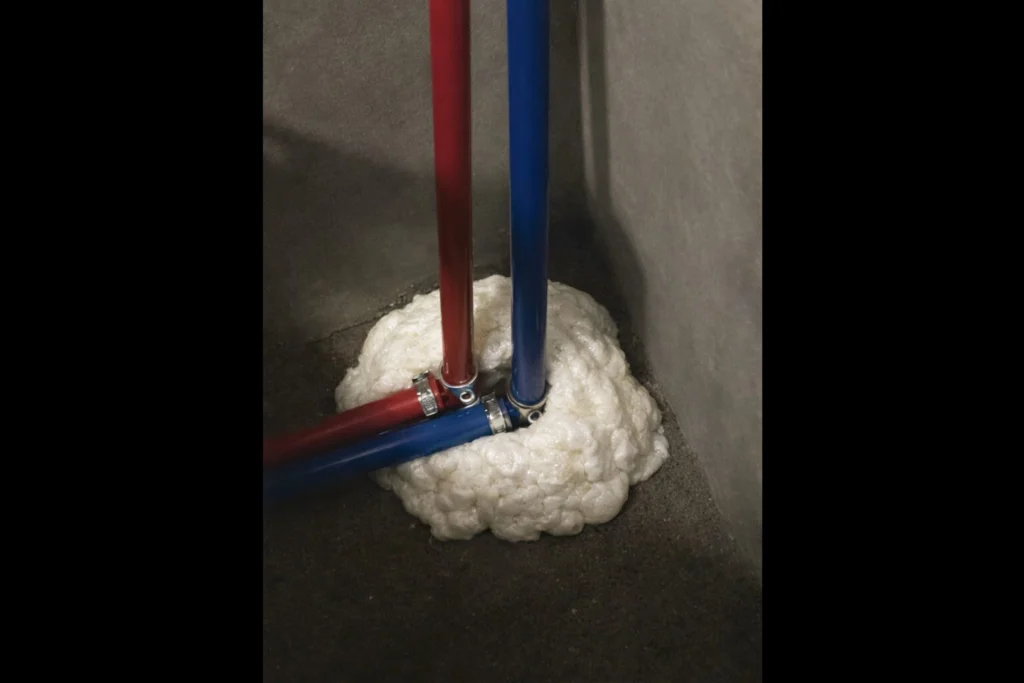 How to Keep Mice Out of Your RV (Simple Prevention Tips That Actually Work) 2 Red and blue RV PEX water lines passing through a floor opening sealed with expanding foam insulation to prevent mice from entering an RV.